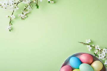 Happy Easter. Dyed Easter eggs on rustic table with cherry blossom tree branch on green background. Easter holiday card background with copy space. Top view.