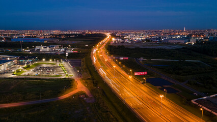 Aerial above view of the bigger highway with bigger traffic cars next to forest and the historical and at same time modern city of St. Petersburg at light summer night
