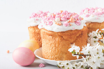 Traditional Easter sweet bread or cakes with white icing and sugar decor, colored eggs and cherry blossom tree branch over white table. Various Spring Easter cakes. Happy Easter day. Selective focus.