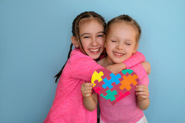 A cute beautiful girl hugs her sister with autism syndrome holding a heart-shaped card. Caring,...
