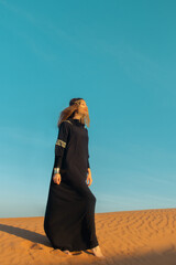 Beautiful woman in brilliant Burqa mask among the Dubai desert at sunset timeArabian style.