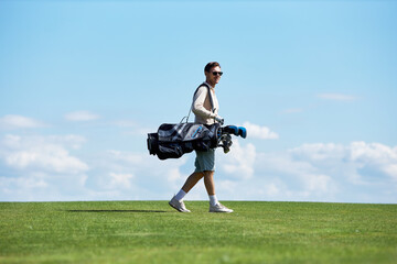 Minimal side view portrait of rich sporty man carrying golf bag walking on green field against sky,...