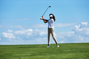 Minimal full length portrait of sporty young woman playing golf on green field against sky and...