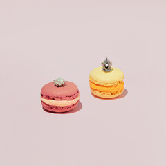 Two macarons, pink and yellow,  cookies decorated with miniature jewelry on a pastel background.