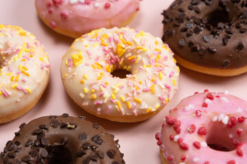 Lots of little donuts with white, pink and chocolate glaze on a pink background, top view