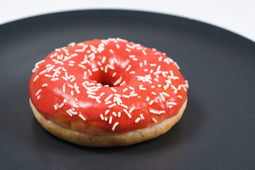 Large doughnut with red glaze and sprinkled on a black background