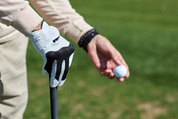 Close up of male hand holding golf ball outdoors against green grass, copy space