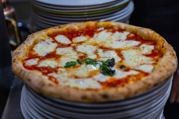Pizza Margherita tradizionale napoletana a ruota di carro condita con sugo di pomodoro, mozzarella di bufala e basilico fresco appena cotta nel forno a legna e pronta per essere servita