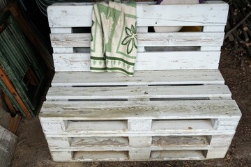 Alte weiße Holzbank mit grün-weißer Wolldecke mit Muster über Lehne 