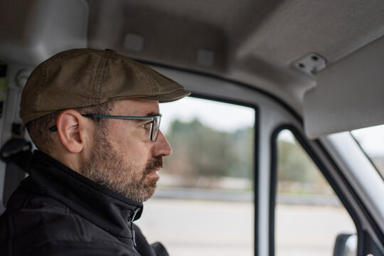 man driving van, white vehicle interior, person in his forties wearing beret and concentrating on driving