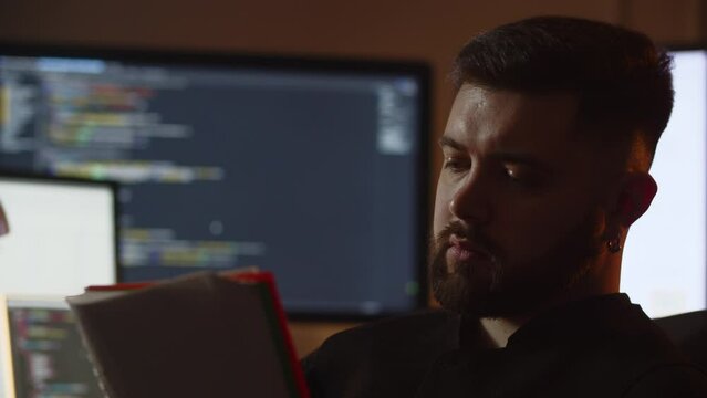 A male programmer makes entries in his notebook. A creative young programmer sitting in front of several monitors is writing down ideas for his new project.