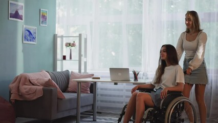 Woman takes sister with disability with traumatic brain injury for walk on fresh air in countryside. Caring lady pushes wheelchair in living room