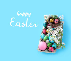 Fototapeta premium Happy Easter greeting card. colorful eggs, nest, cherry flowers in carton box on blue background. Easter holiday concept. symbol of spring festive season.