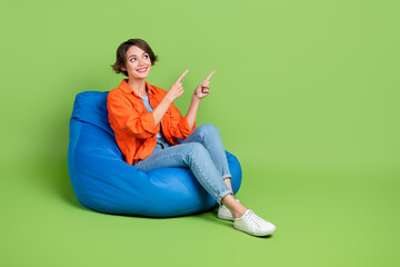 Full length photo of sweet dreamy lady dressed jeans shirt bean bag showing emtpy space isolated green color background