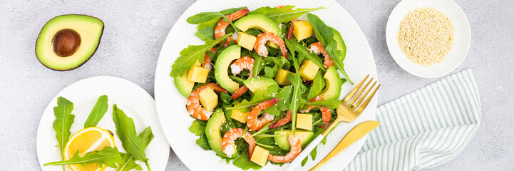Flat lay of Healthy salad plate. Fresh seafood recipe. Grilled shrimps and fresh vegetables (avocado, arugula, mango) on gray concrete background. 