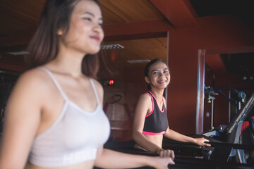 Two pretty asian women talking to each other while brisk walking on the treadmill. Working out or doing cardio inside the gym.