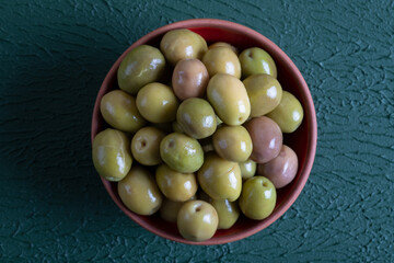 Bowl full of green olives on green background