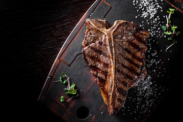 Grilled T-bone Steak on bones on wooden plate on bkack background