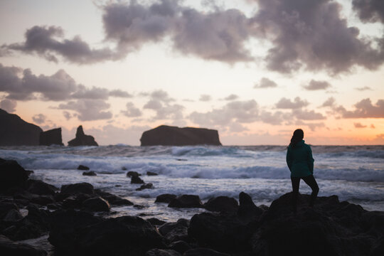 Woman standing on rocky seashore at sunset