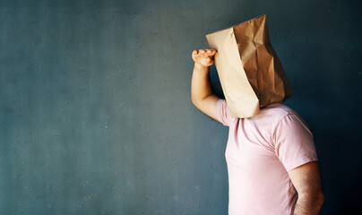Man with a paper bag on head looking far away distance over gray background