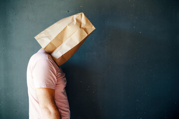 Profile view of upset man with a paper bag on head over gray background with copy space