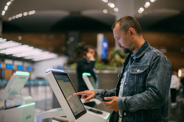 A male passenger at the electronic check-in desk in the departure area of the modern airport terminal.