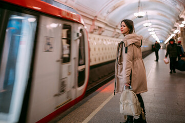 A young woman stands on the platform at the metro station, a train arrives.