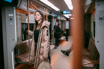 A young woman rides in a modern subway car. A beautiful girl in a jacket rides after work in the subway late