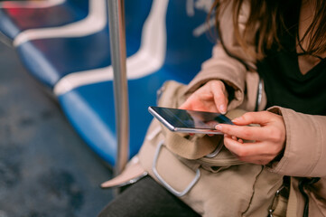 A young woman rides in a modern subway car with a phone in her hands. Close-up of hands with phone