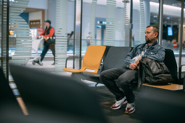 A male passenger is sitting waiting for boarding in the departure area of the modern airport terminal.