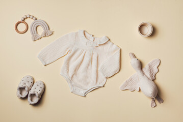 Mockup of cream infant bodysuit made of organic cotton with eco friendly baby accessories, knitted rainbow, soft duck on beige backgroundd. Gift for newborn baby. Top view. Flat lay. Copy space