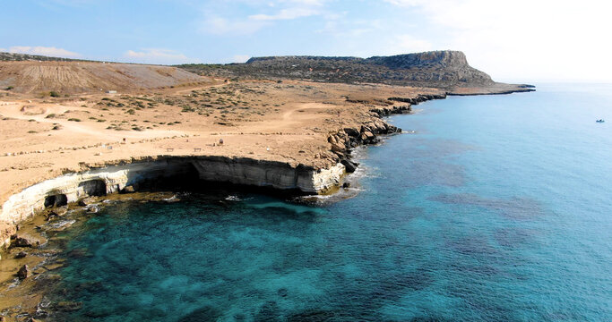 Drone flight over the island's coastline with deserted rocky shore with a steep cliff and the sea with clear water and waves.