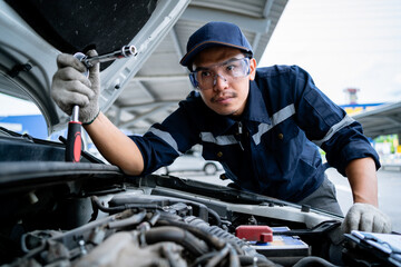 Portrait of an Asian mechanic checking the safety of a car. Maintenance of damaged parts in the garage. Maintenance repairs. Repair service concept.