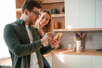 Man showing some media to woman on the phone. Young couple is on the kitchen together