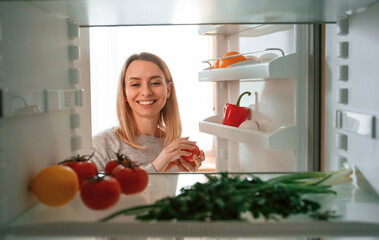 Taking the vegetables from fridge. Beautiful young woman is on the kitchen