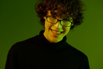 Fototapeta premium Man young man portrait close-up portrait in glasses fashion smile, hipster lifestyle, portrait green background mixed neon light, copy space
