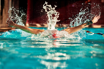 A man with a red cap swims in a blue pool, head-on shot