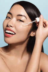 Young asian beauty woman, applied vitamin c serum, holds dropper near face and smiles, using...