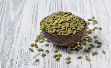 Pumpkin seeds in a wooden cup on a white wooden background. Rustic style. The concept of vegetarian and diet snacks