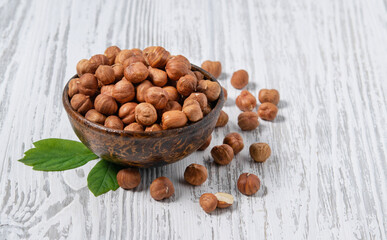 Hazelnuts raw and peeled in a wooden cup on a white wooden background. Rustic style.