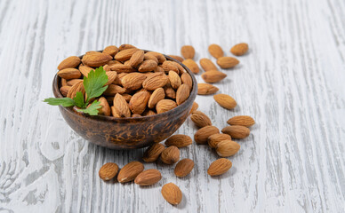 Raw almonds in a wooden cup on a white wooden background. Rustic style. The concept of vegetarian and diet snacks.