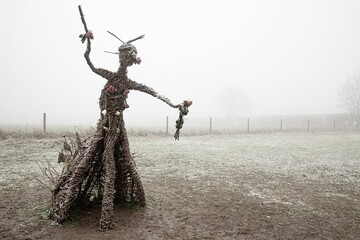Pagan wicker witch adorned with roses at The Rollright Stones in Oxfordshire on a misty winter day