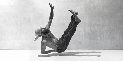 Black and white image, monochrome. Levitation. Falling down. Muscular bearded man training shirtless against textured background. Art of movement, male body aesthetics, health, sport concept