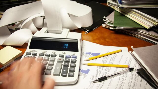Time lapse of a man's hand using a calculator on a cluttered office desk.