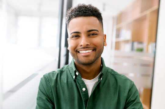 Close-up portrait of a happy indian young man with friendly wide toothy smile, latin guy wearing casual ggreen shirt looks into camera, employee profile photo