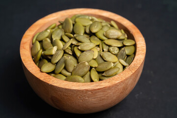 Pumpkin seeds in a wooden bowl on a dark background