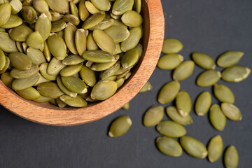 Pumpkin seeds in a wooden bowl on a dark background