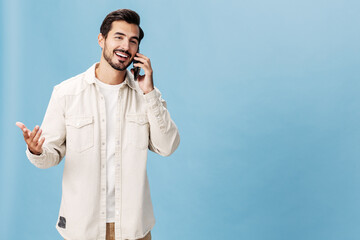 Fototapeta na wymiar Portrait of a man brunette animation and joy talking on the phone smile with teeth, on a blue background in a white T-shirt and jeans, copy space