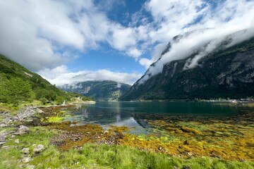 Naklejka na ściany i meble Drone shot of the lake surrounded by cloud-covered green hills at Geiranger Fjord, Norway