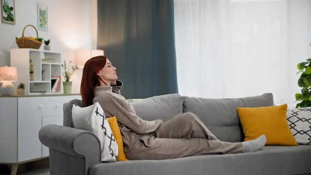 cute woman relaxing at home meditating in silence sitting on couch in a cozy room background of window